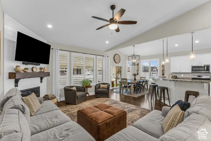 Open-concept interior featuring vaulted ceilings, a gas fireplace with a rustic wood mantel, shiplap accent wall, wood-finish flooring, and a kitchen island with pendant lighting
