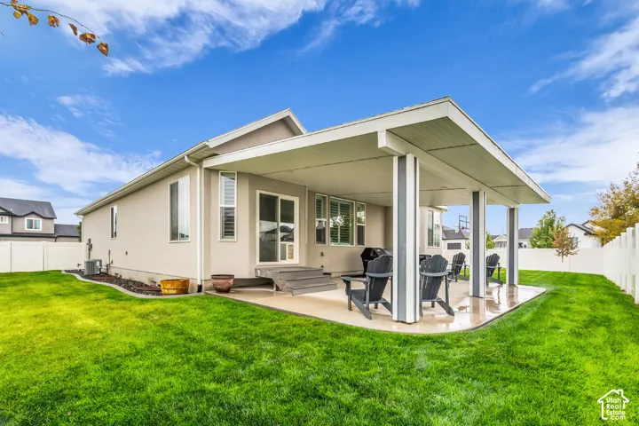 Covered concrete patio with structural support columns, exterior siding, sliding glass door, and a fenced backyard with landscaped edging