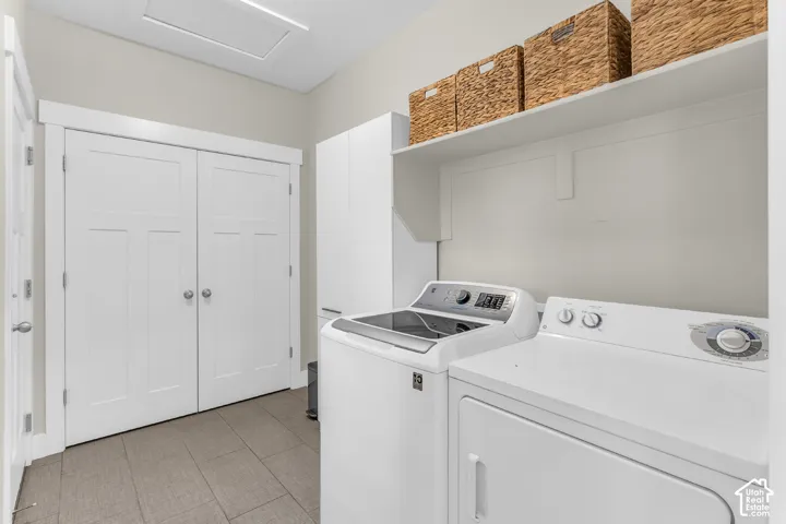 Utility room featuring ceramic tile flooring, white shaker-style cabinetry, double-door closet storage, and overhead open shelving