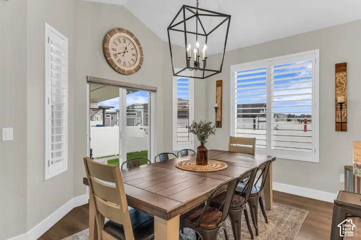 Vaulted ceiling featuring a geometric metal pendant light, wood-finish flooring, plantation shutters, and sliding glass door