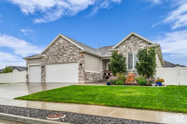 Exterior facade featuring stone veneer detailing, a multi-gabled roofline, a three-car garage, and vinyl privacy fencing