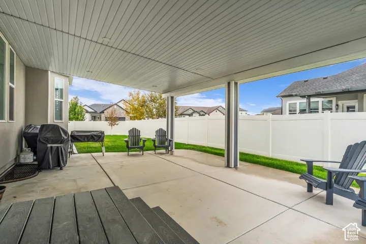 Covered concrete patio featuring recessed lighting, support columns, and a white vinyl privacy fence enclosing the lawn