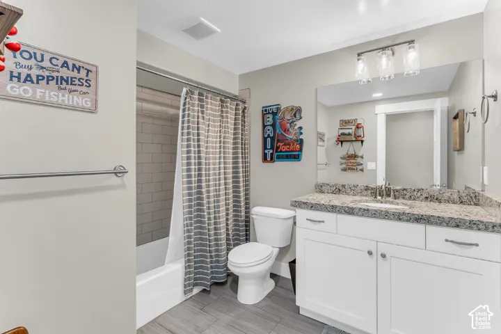 Bathroom featuring a white vanity with a stone-look countertop, an undermount sink, a tub-shower combination with horizontal tile surround, and wood-finish flooring