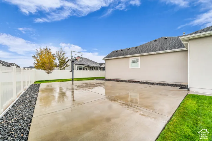 Concrete patio featuring a perimeter of decorative rock, a white vinyl privacy fence, and a built-in basketball hoop