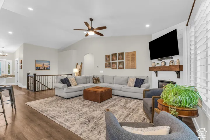Vaulted ceilings, wood-finish flooring, fireplace with a custom wood mantel, recessed lighting, and a ceiling fan with integrated light fixture
