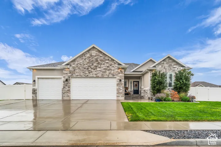 Single-story exterior featuring multi-textured stone veneer, dual garage bays, concrete driveway, and white vinyl perimeter fencing