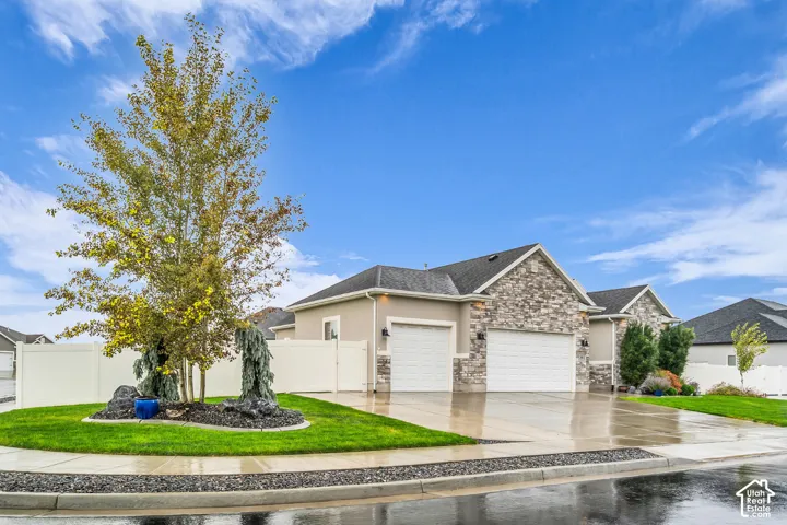 Exterior facade featuring stone veneer detailing, a multi-car garage, and low-maintenance landscaping with mature trees