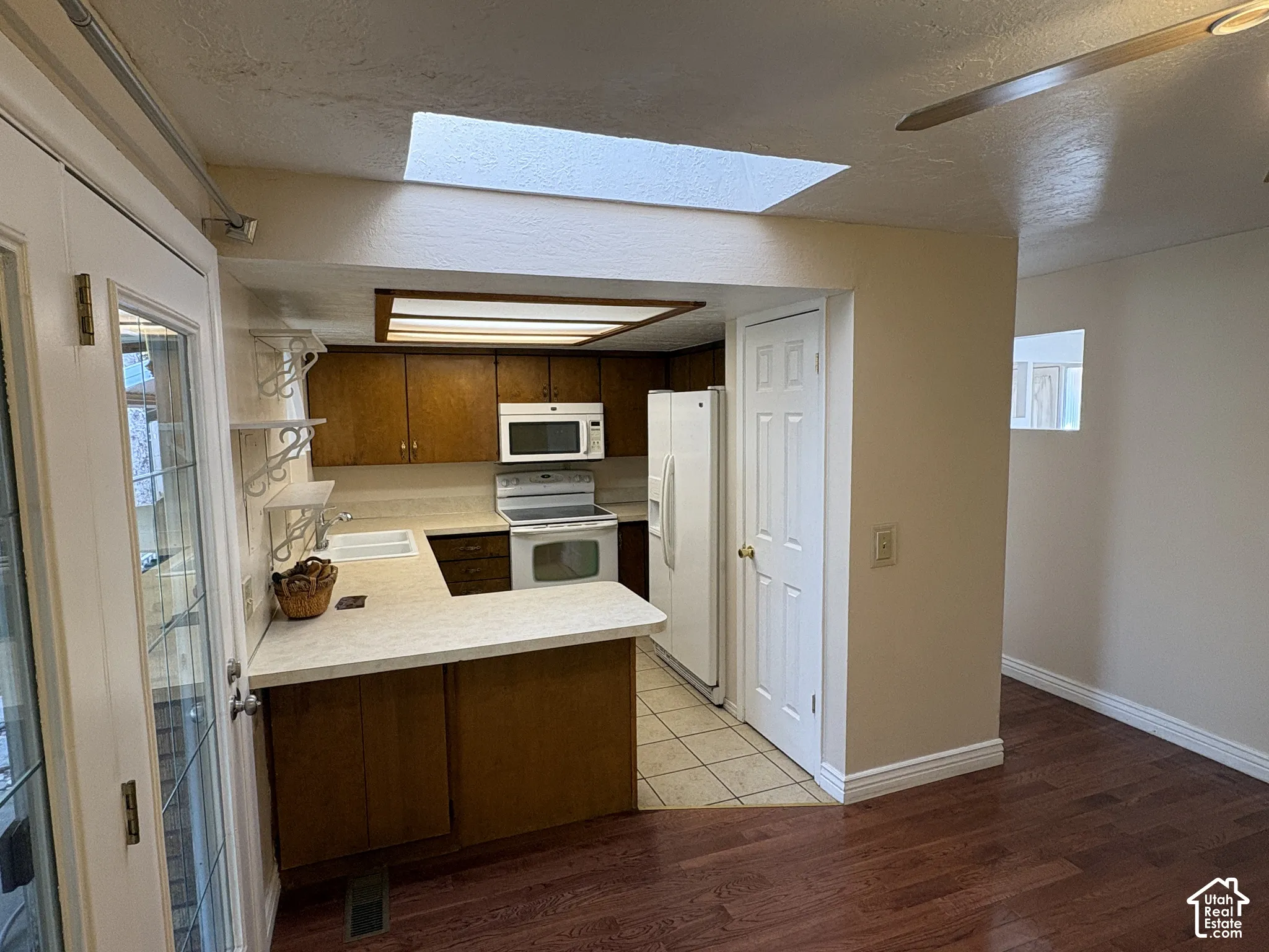 Kitchen featuring wood cabinetry, solid-surface countertops, tile flooring, integrated ceiling lighting, and a skylight