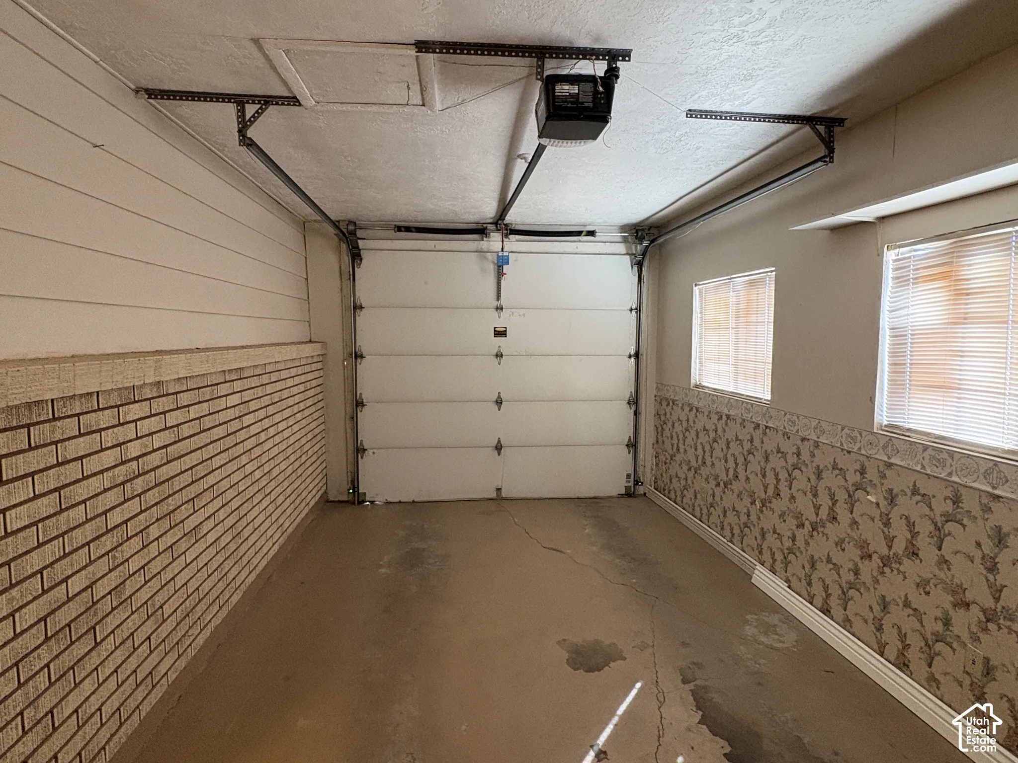 Enclosed garage featuring an automated overhead door, textured walls, and dual side windows