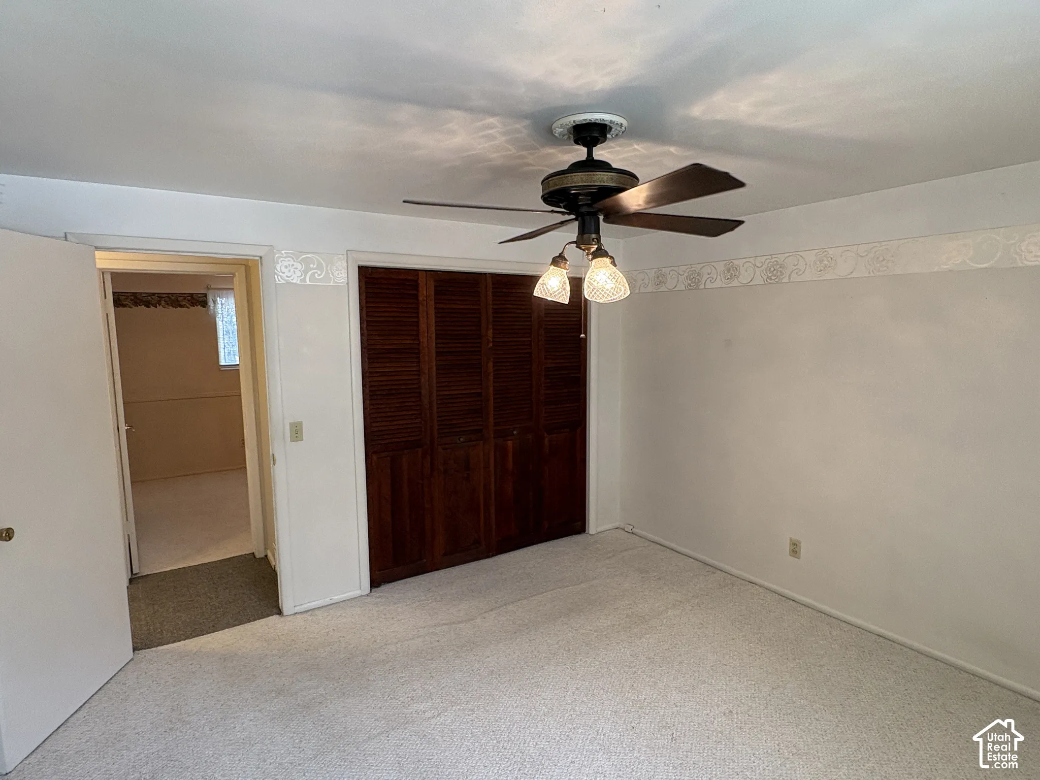 Room interior featuring wood-finish louvered closet doors, ceiling-mounted paddle fan with integrated lighting, and decorative wall border