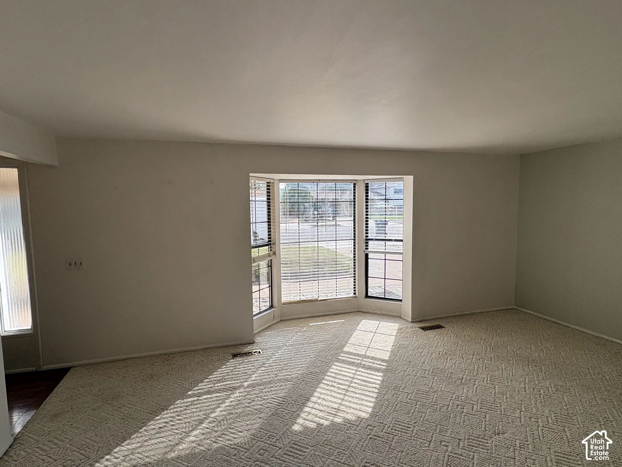 Spacious interior featuring a large bay window, neutral carpeting, and a sidelight window with textured glass