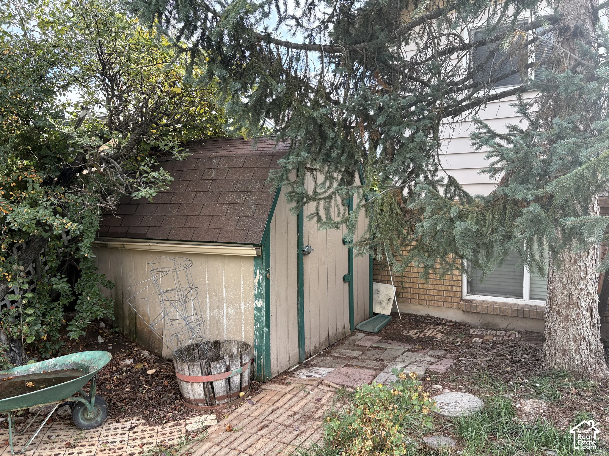 Storage shed with an asphalt shingle roof, wood-panel exterior, brick veneer foundation, and a brick paver walkway
