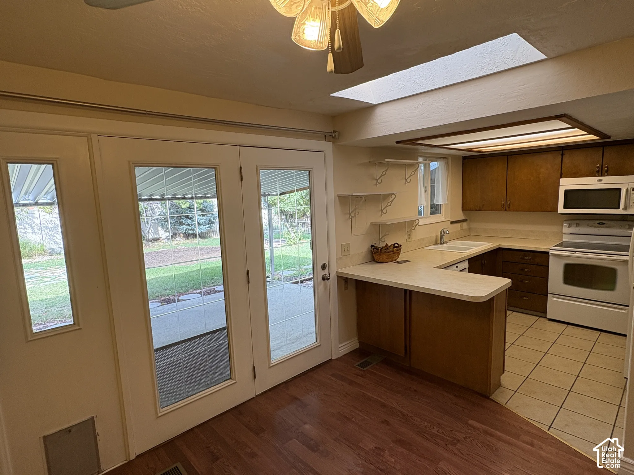 Kitchen featuring wood-finish cabinetry, light-toned countertops, a skylight, tile flooring, and double glass doors
