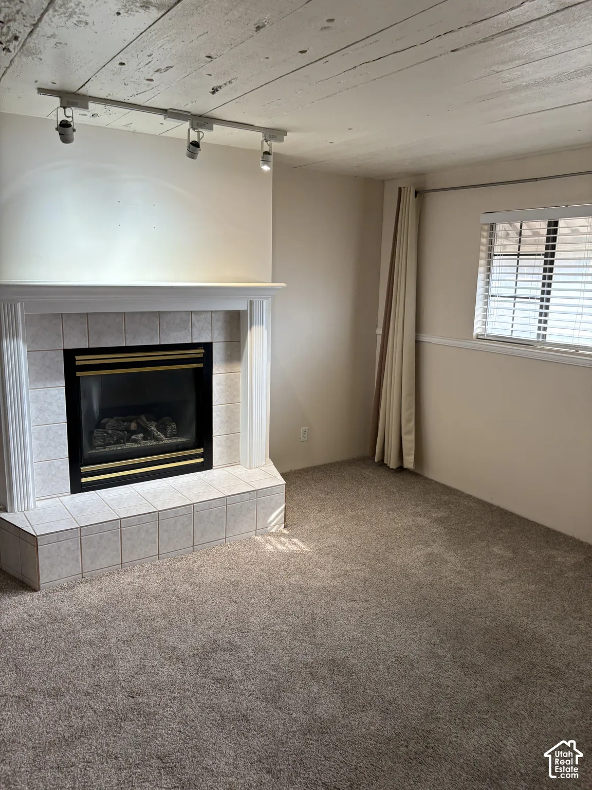 Fireplace with a tile surround and mantel, wood-plank ceiling, adjustable track lighting, and carpeted flooring