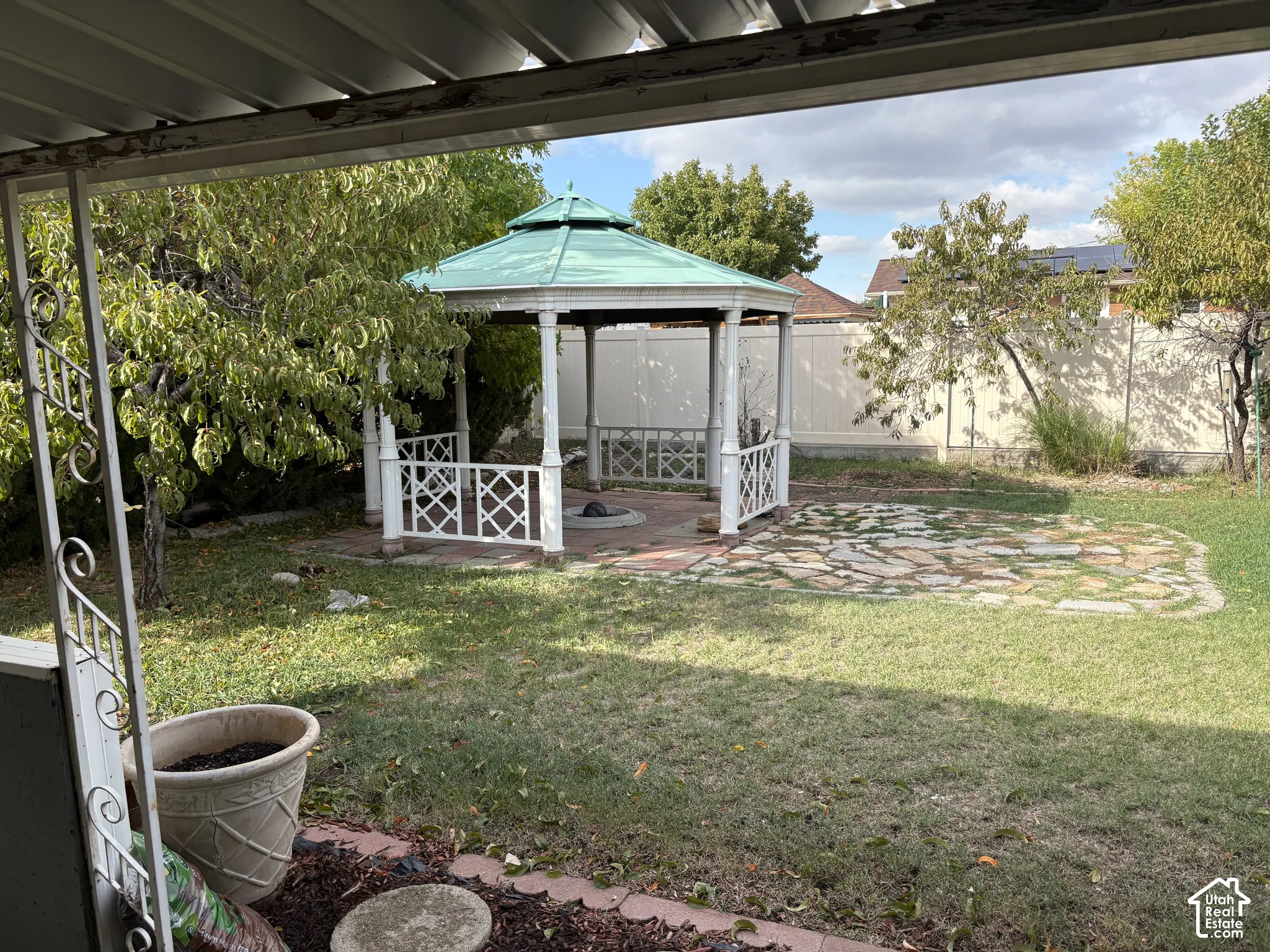 Backyard featuring a green-roofed gazebo, stone paver patio, and lawn area enclosed by perimeter fencing