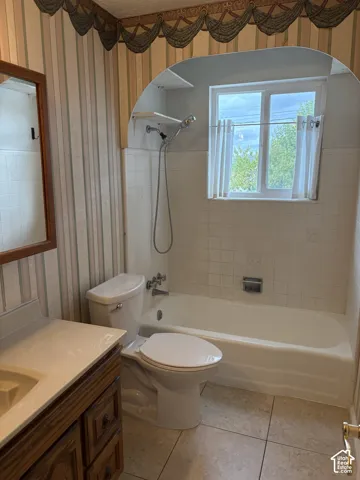 Full bathroom featuring a white porcelain tub with tile surround, an arched alcove, a wood-finish vanity with an integrated sink, and large-format tile flooring