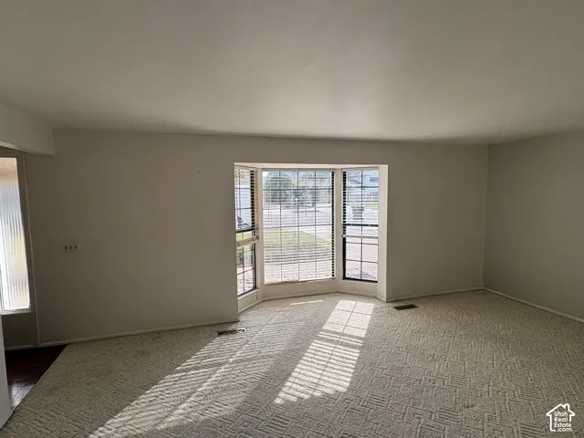 Spacious interior featuring a large bay window, neutral carpeting, and a sidelight window with textured glass
