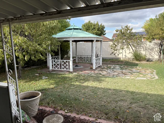 Backyard featuring a green-roofed gazebo, stone paver patio, and lawn area enclosed by perimeter fencing