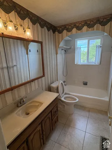 Bathroom featuring a wood-finish vanity with a drop-in sink, a built-in medicine cabinet, an arched shower surround with tile walls, and large-format tile flooring
