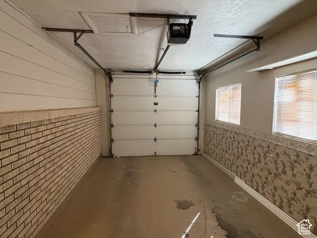 Enclosed garage featuring an automated overhead door, textured walls, and dual side windows