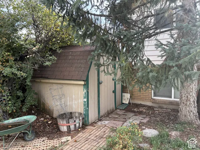 Storage shed with an asphalt shingle roof, wood-panel exterior, brick veneer foundation, and a brick paver walkway