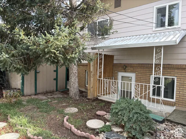 Exterior featuring multi-level brick and horizontal siding, covered entryway with ornamental metal railing, and landscaped grounds with mature coniferous trees and stone paver accents