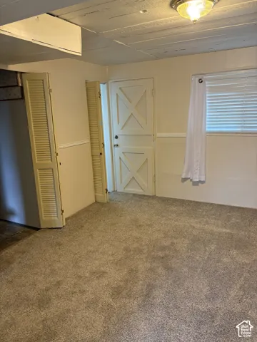 Interior room featuring textured ceiling with integrated flush-mount lighting, wall-to-wall carpeting, louvered bi-fold closet doors, and a decorative cross-buck paneled door