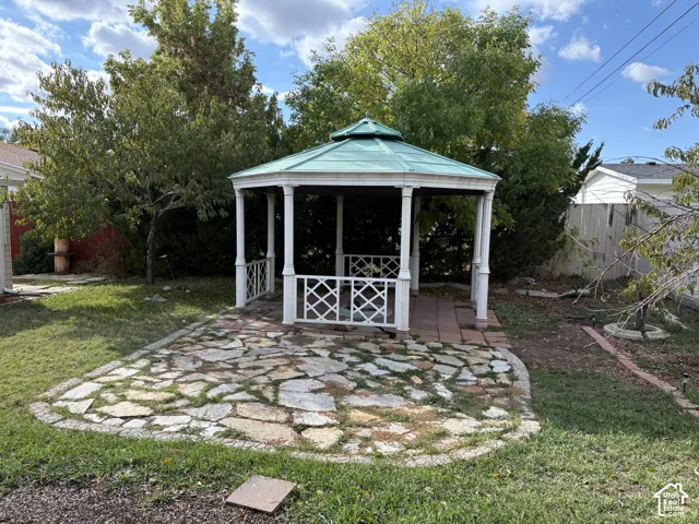 Octagonal gazebo featuring a metal roof, white decorative lattice railings, and classical columns, set upon a natural stone patio