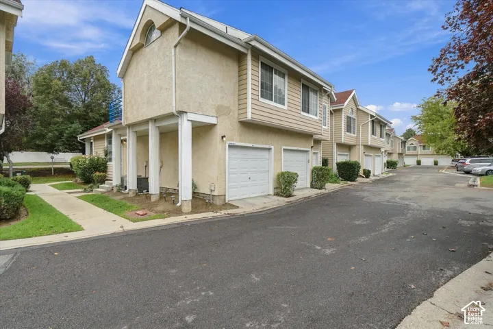 Multi-unit residential exterior featuring a stucco and horizontal siding facade, gable rooflines, arched window accents, and attached multi-car garages