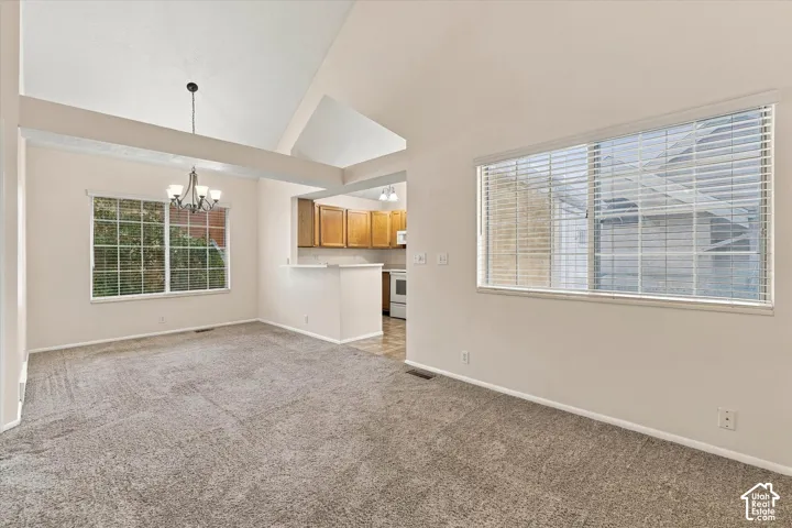 Vaulted ceilings, view of dining area with large windows, built-in light fixture, and a pass-through opening to the kitchen area