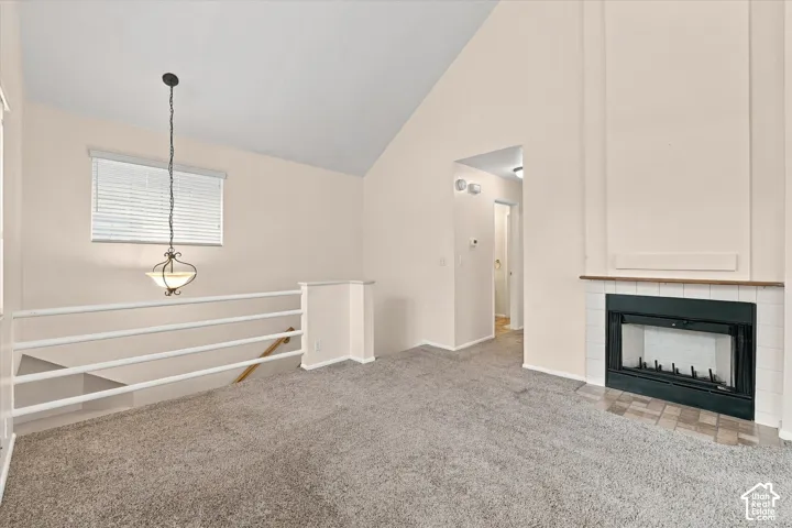 Vaulted ceilings featuring a fireplace with tile surround, carpeted flooring, and a decorative pendant light fixture