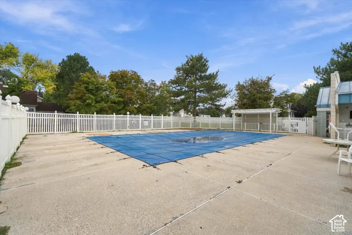 In-ground swimming pool with protective cover, expansive concrete deck, white vinyl privacy fencing, and wooden pergola structure