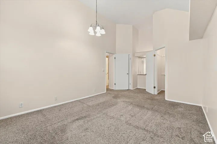 Primary Bedroom with vaulted ceilings, neutral wall palette, carpeting, and multi-light pendant fixture