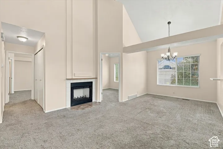 Vaulted ceilings with exposed beam, fireplace surround with tile hearth, multi-pane window, and classic chandelier fixture