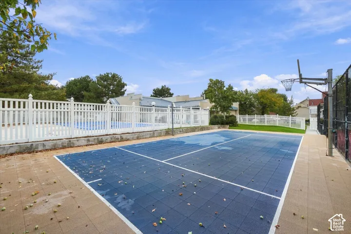 Outdoor multi-purpose court with modular surfacing, basketball hoop, white vinyl perimeter fencing, and adjacent swimming area