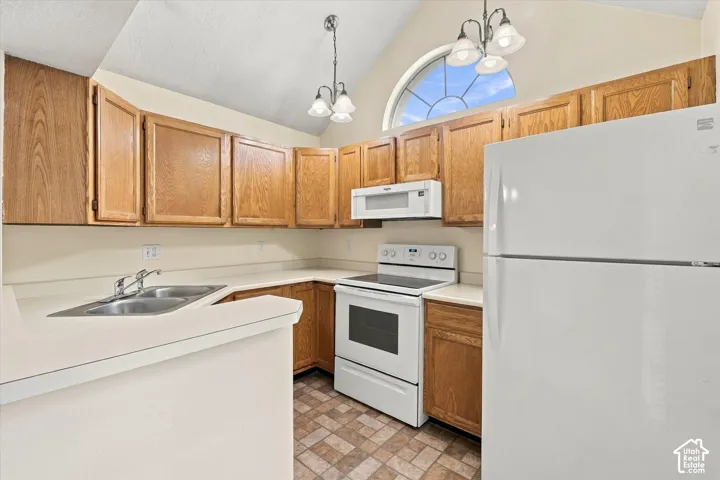 Kitchen featuring vaulted ceilings, wood-finish cabinetry, white appliances, a double-basin stainless steel sink, and a semi-circular arched window