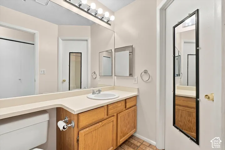 Bathroom featuring wood-finish cabinetry, a white countertop with an integrated basin, a large wall-spanning mirror, and multi-bulb vanity lighting