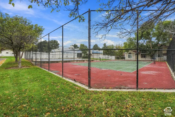 Private tennis court featuring a multi-color surface, chain-link perimeter fencing, and mature landscaping