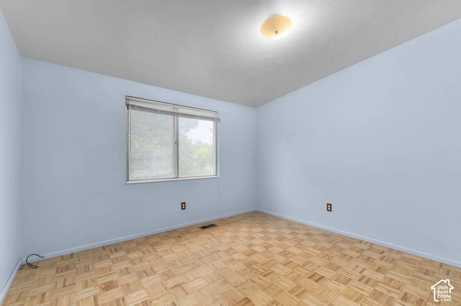 Room featuring parquet wood-finish flooring, a window with horizontal blinds, and a dome-style flush-mount ceiling light