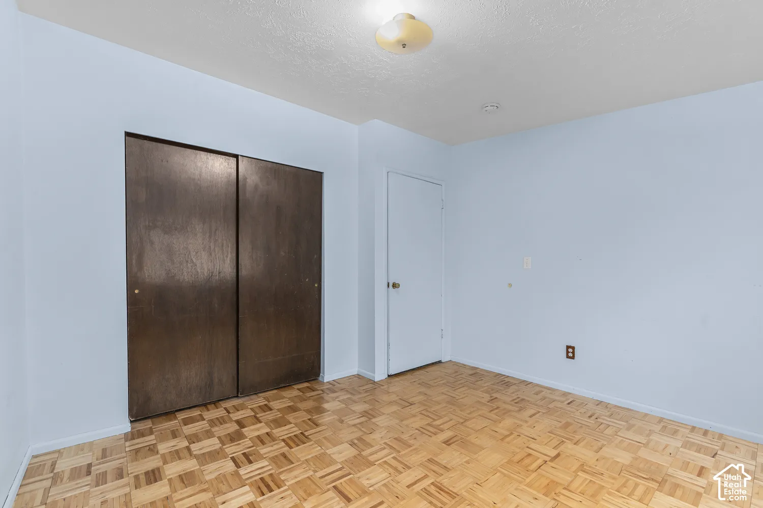 Room featuring wood-finish parquet flooring, dual sliding wood-grain closet doors, and a central ceiling-mounted light fixture