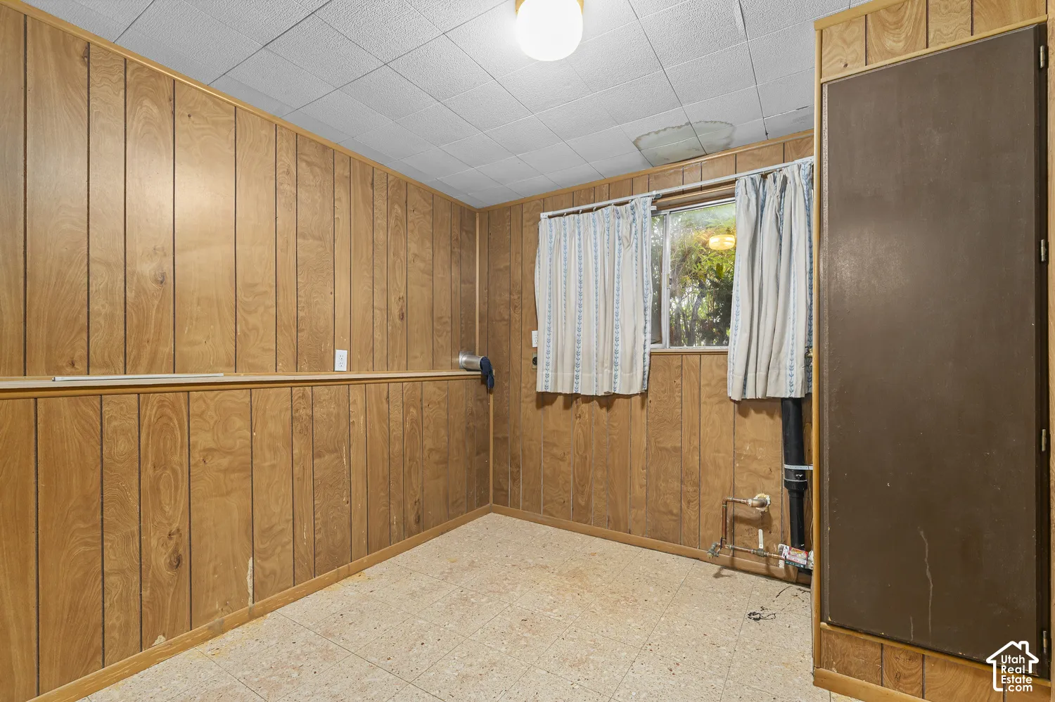 Room featuring wood-paneled walls, a drop ceiling, tile flooring, and a built-in storage cabinet