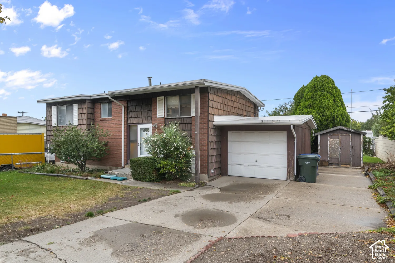 Split-level exterior featuring brick and shake-style siding, attached single-car garage, concrete driveway, and detached storage structure