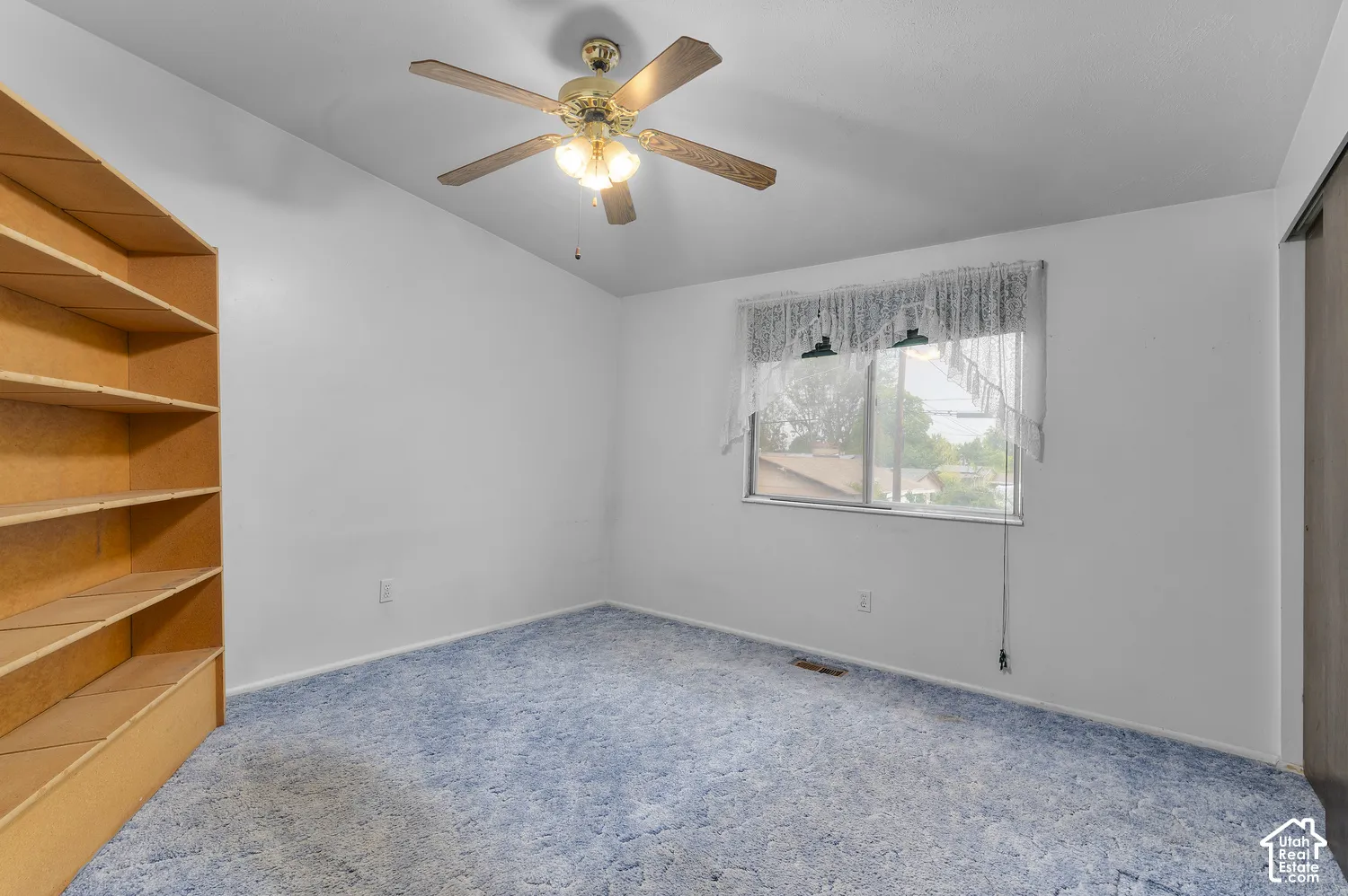 Vaulted ceiling room featuring built-in floor-to-ceiling shelving, blue carpeting, and a central ceiling fan with integrated lighting
