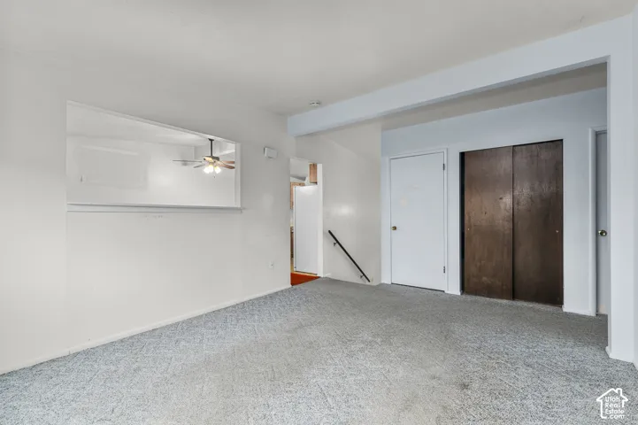 Neutral-toned carpeting, pass-through wall opening, dark wood-finish sliding closet doors, and a metal handrail