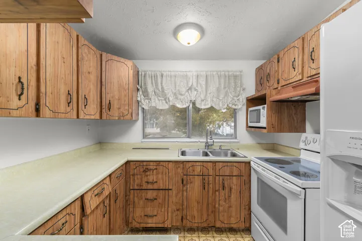 Kitchen featuring wood-finish cabinetry, solid-surface countertops, dual-basin stainless steel sink, and built-in microwave shelf