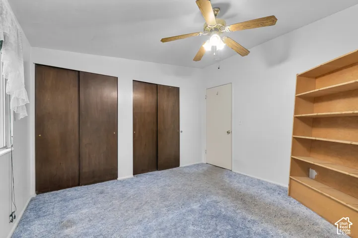 Room featuring two sets of dark wood-finish sliding closet doors, built-in open shelving, carpeted flooring, and a ceiling-mounted fan with integrated lighting