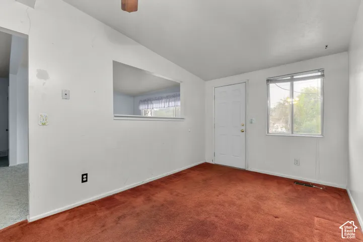Interior space featuring carpeted flooring, a pass-through window cutout, a single-panel exterior door, and a multi-pane window