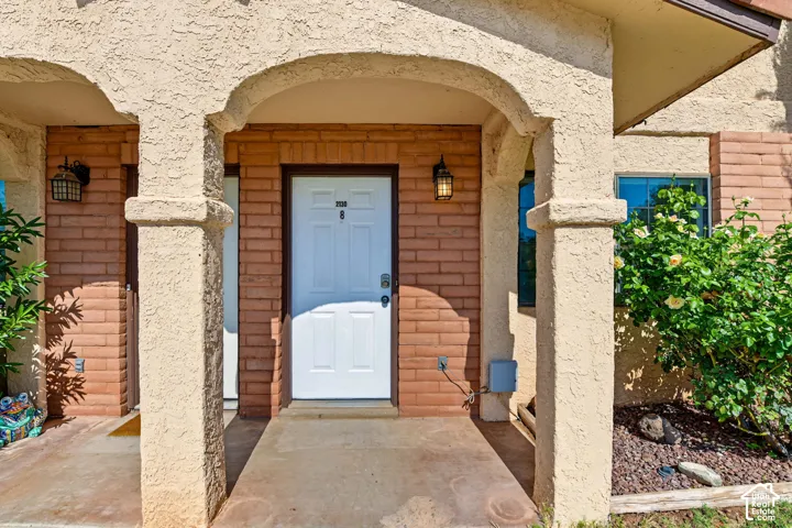 Covered porch featuring arched stucco supports, red brick masonry detailing, and dual exterior wall-mounted light fixtures