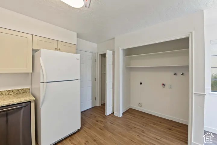 Kitchen featuring light-toned cabinetry, stone-finish countertops, wood-finish flooring, and a dedicated laundry area with integrated shelving