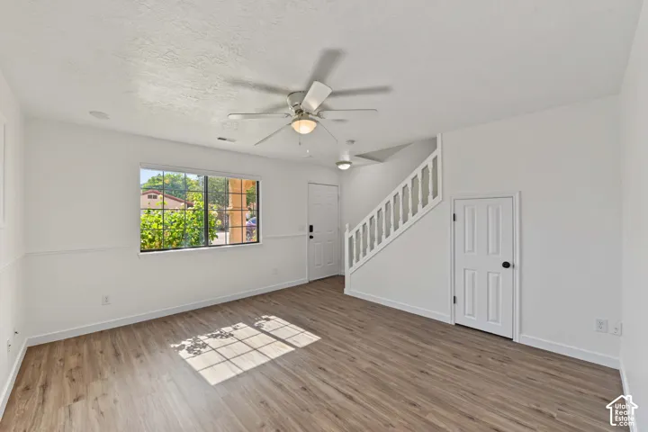Interior space featuring wood-finish flooring, chair rail molding, a ceiling fan with integrated lighting, and a white staircase with a decorative balustrade